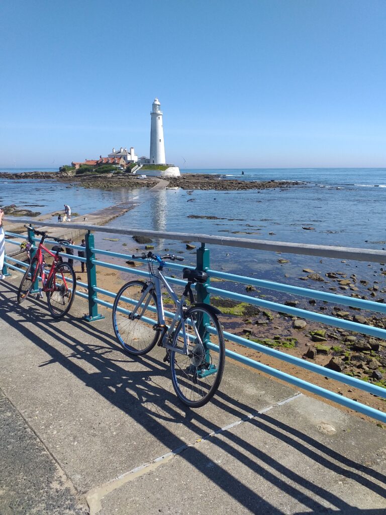 two bikes propped against a fence, with sea and a lighthouse in the background